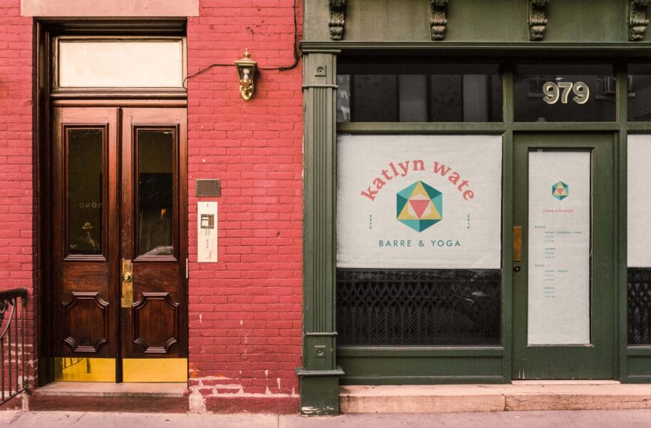 View of the Katlyn Wate logo on the glass window of a brick building storefront. A sample class schedule is listed on a glass door with a roller shade drawn shut.